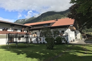 A two-story building with a red-tiled roof, a covered outdoor seating area, and a mountain backdrop.