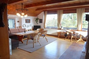 A cozy living room with a wooden ceiling, a dining table with chairs, a sofa, and a large window with curtains. - Holiday apartment in Altendorf with Wi-Fi (Altendorf)