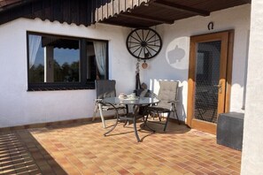 A patio with a round table and chairs, a window with curtains, a wooden door, and a decorative wheel. - Holiday apartment in Altendorf with Wi-Fi (Altendorf)
