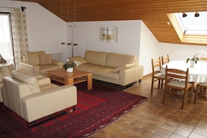 Ein Wohnzimmer mit einer Couch, Sesseln, einem Couchtisch und einem Esstisch mit Stühlen.