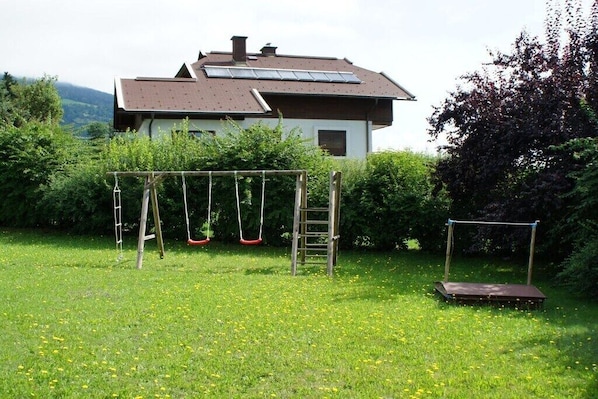Ein Haus mit Solardach, Schaukel und einem Garten mit Gras und Löwenzahn.