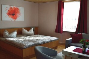 Quarto com cama, uma cadeira, uma mesa e janela com cortinas.