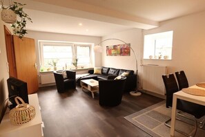 Ein Wohnzimmer mit einer Couch, Sesseln, einem Couchtisch, einem Esstisch und einem Heizkörper.