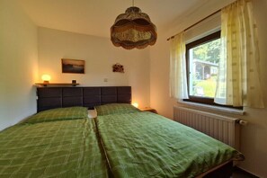 Ein Schlafzimmer mit Bett, Fenster mit Vorhängen, einer Wandlampe und einem Bild.