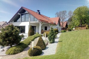 Ein modernes, zweistöckiges Haus mit einem geneigten Dach, einem gepflegten Rasen und ordentlich geschnittenen Hecken.