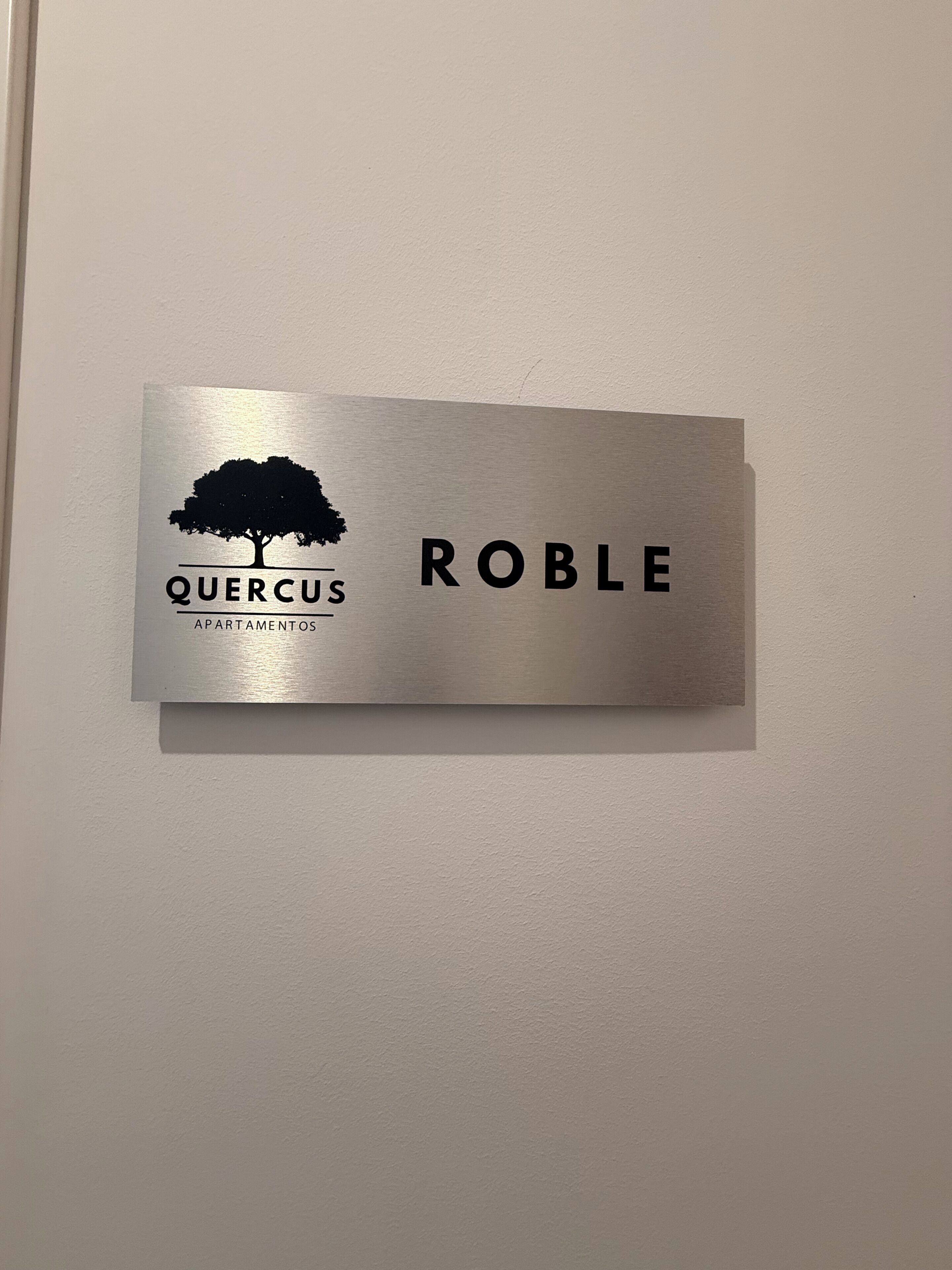 Een metalen bord met een boom silhouet en de tekst 'QUERCUS APARTAMENTOS ROBLE'.