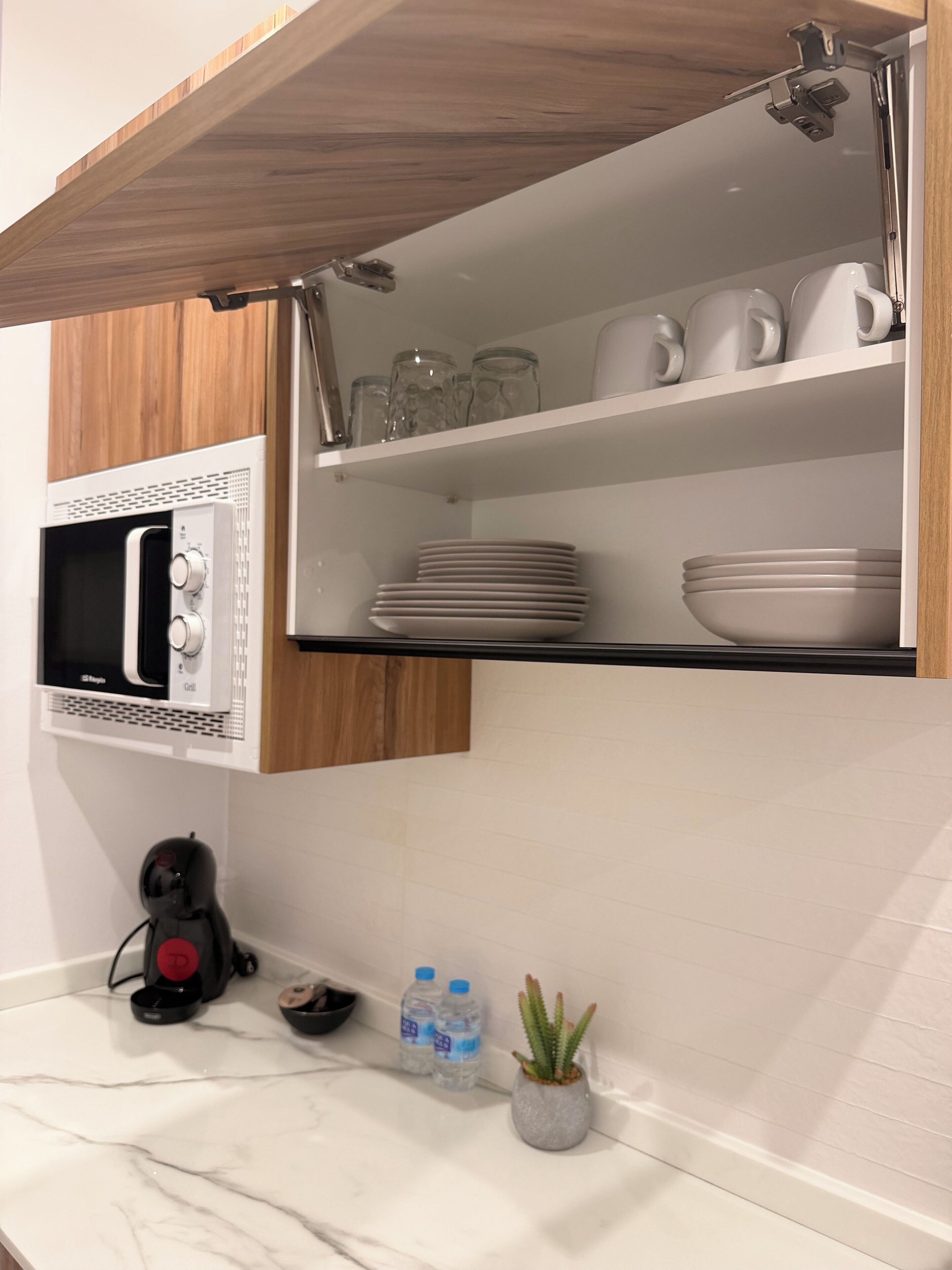 A kitchen with a microwave, a coffee maker, a water dispenser, and a potted plant.