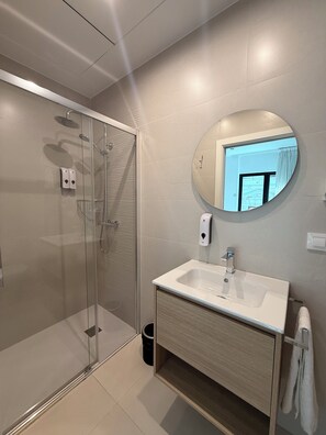 Un bagno moderno con box doccia in vetro, uno specchio rotondo e un lavandino bianco.