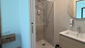 A modern bathroom with a glass-enclosed shower, a sink with a mirror, and a wooden shelf.