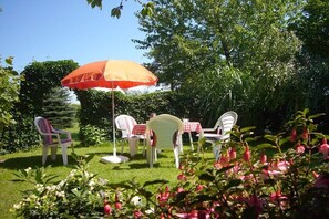 Ein Garten mit Sitzgelegenheiten im Freien, darunter Stühle und ein Tisch, unter einem großen Sonnenschirm.