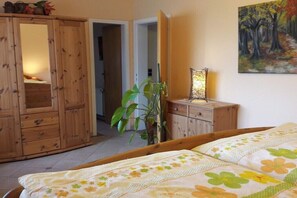Ein Schlafzimmer mit einem Bett, einem Holzschrank, einer Pflanze und einem Bild an der Wand.
