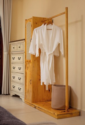 Ein hölzerner Kleiderschrank mit Kleiderstange, einem weißen Bademantel und einem Korbwäschesammler.