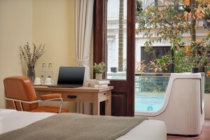 Ein Hotelzimmer mit Holzschreibtisch, einem Laptop, einem Stuhl, einem Bett und einem Fenster mit Blick auf einen Pool und Bäume.