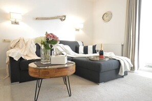 Ein modernes Wohnzimmer mit einer Couch, einem runden Couchtisch, einer Blumenvase, einer Uhr und einer Heizung.