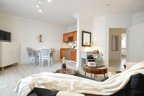 Ein modernes Wohnzimmer mit einer Couch, einem Essbereich mit Stühlen, einer Küche mit Holzschränken und einem an der Wand befestigten Fernseher.