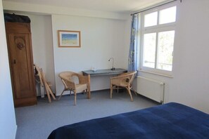 A bedroom with a bed, a desk, two wicker chairs, a radiator, a window with curtains, and a door. - Holiday apartment with 3 bedrooms (Graal-Müritz)