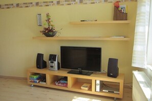 A living room with a flat-screen TV, two speakers, a bookshelf, and a radiator. - Holiday apartment with 3 bedrooms (Graal-Müritz)