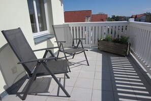 A balcony with two folding chairs, a wooden planter with plants, and a white fence. - Holiday apartment with 3 bedrooms (Graal-Müritz)