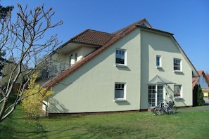 Ein zweistöckiges Gebäude mit Satteldach und einer kleinen Veranda, vor dem ein Fahrrad abgestellt ist.