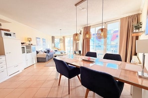 Ein modernes Wohnzimmer mit einer Couch, Esstisch, Stühlen und einer Küchenzeile mit Schränken und einer Mikrowelle.