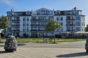 Ein mehrstöckiges Hotel mit Balkonen, einem zentralen Eingang und einer gepflasterten Fläche mit Blumenarrangements.