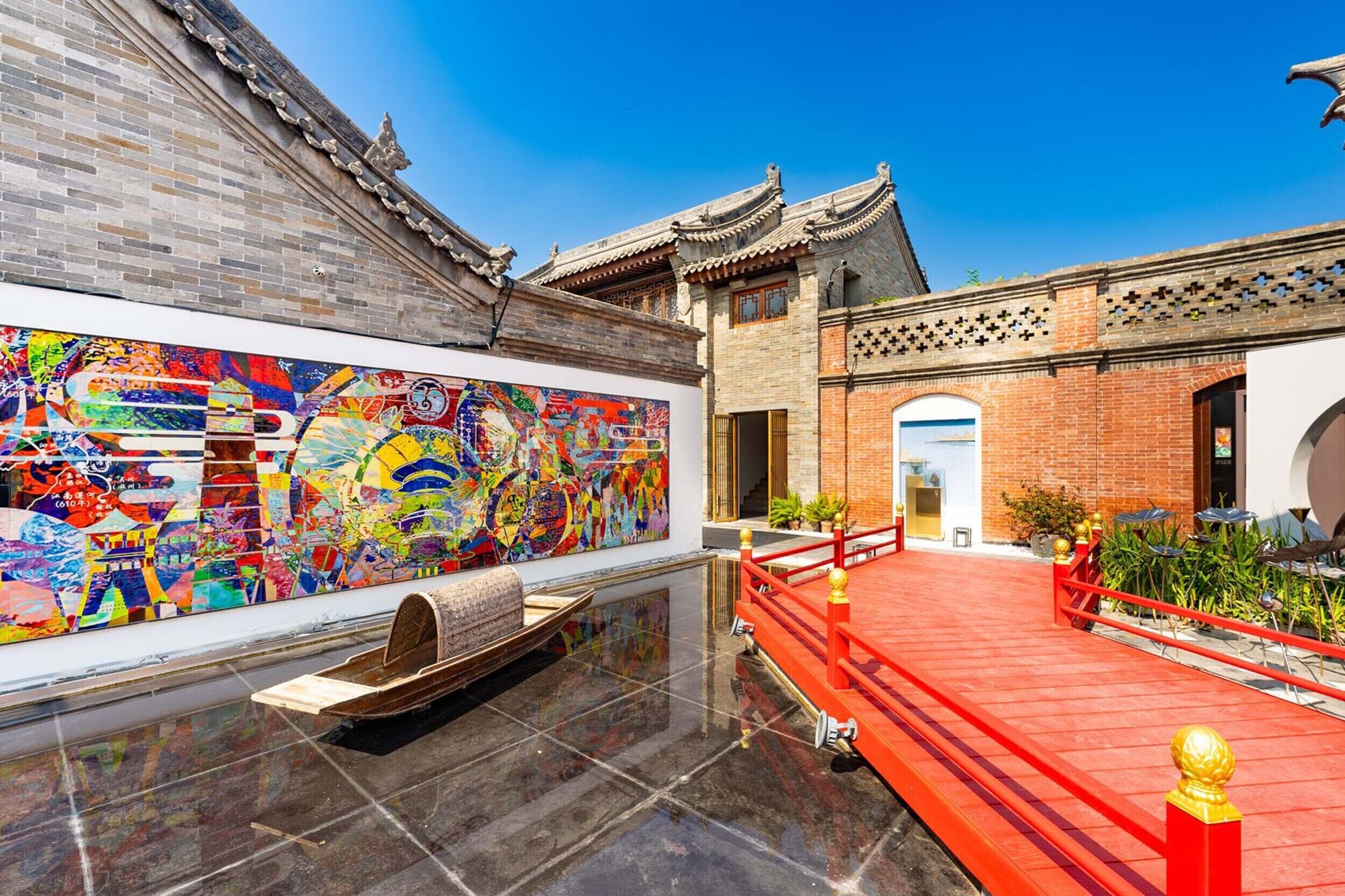 Un patio tradicional chino con suelo de baldosas, un puente rojo y un mural colorido en la pared.