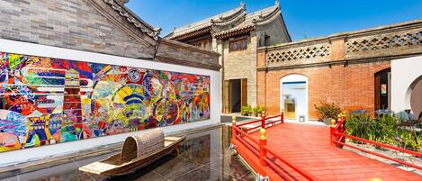 Un patio tradicional chino con suelo de baldosas, un puente rojo y un mural colorido en la pared.