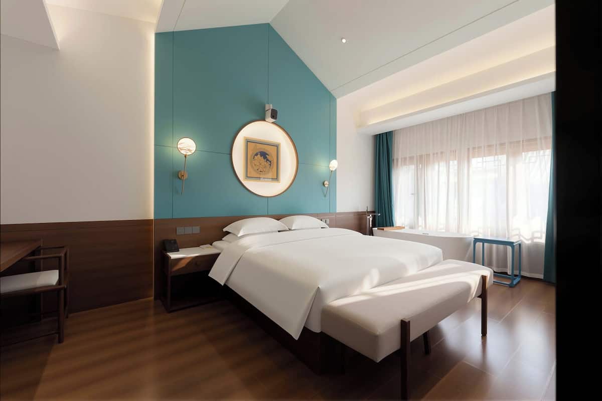 Una habitación de hotel moderna con una cama grande, un escritorio, una silla y una ventana con cortinas.