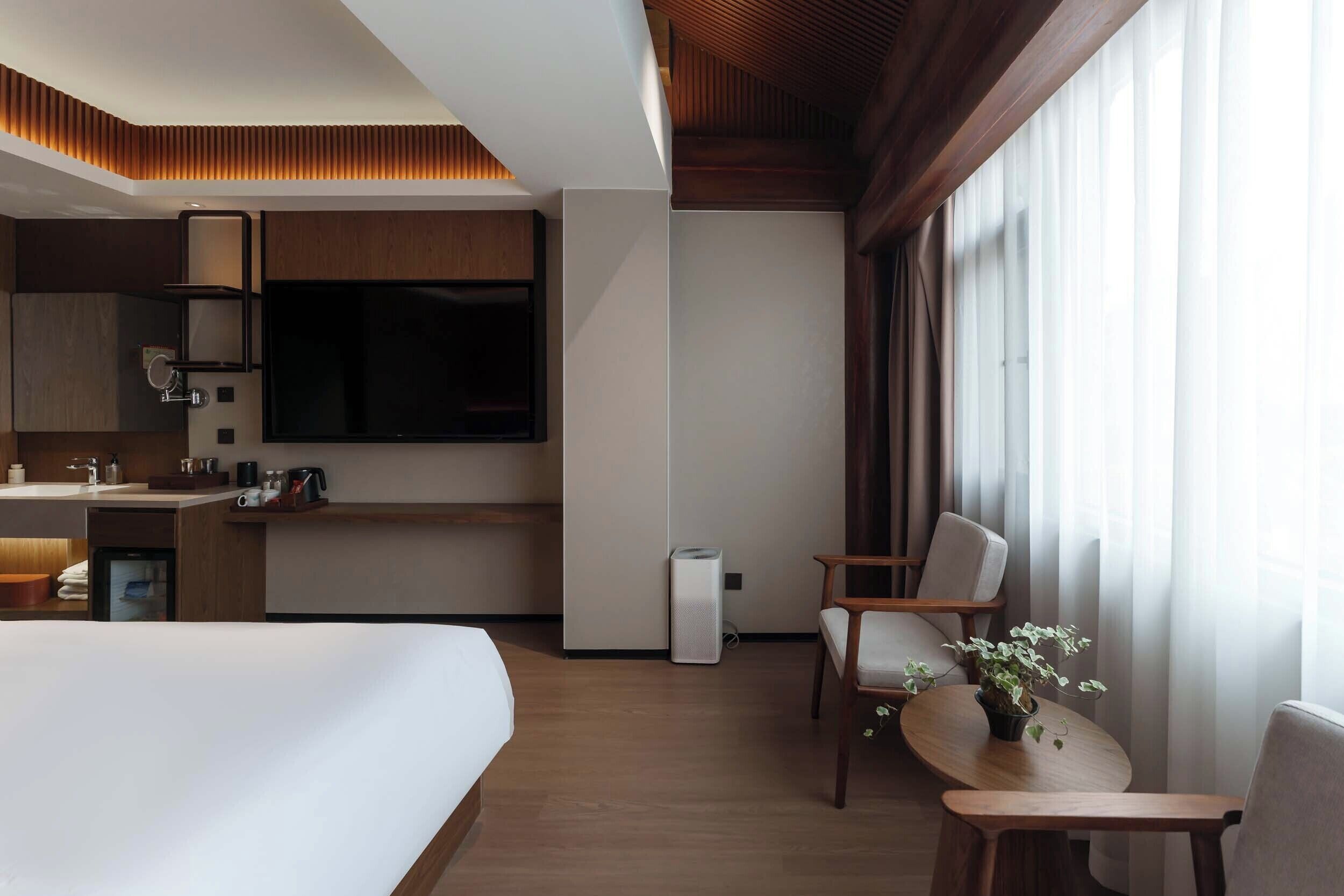 Une chambre d’hôtel avec un lit, une petite table avec une plante, une chaise, un téléviseur et une kitchenette.