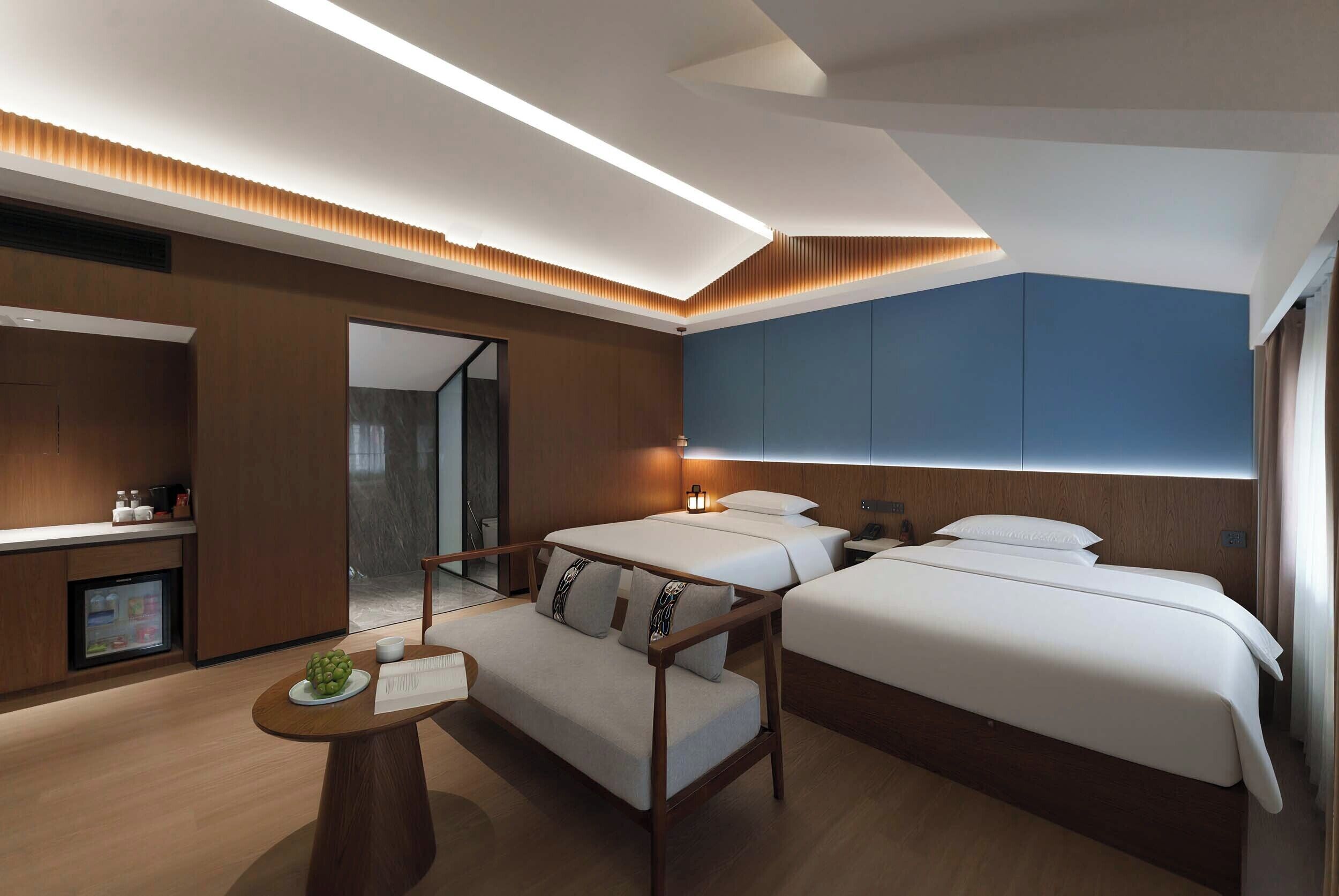 A modern hotel room with a sofa, two beds, a desk, and a TV.