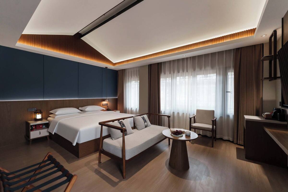 Una habitación de hotel moderna con cama, sofá, escritorio, silla y una mesita.