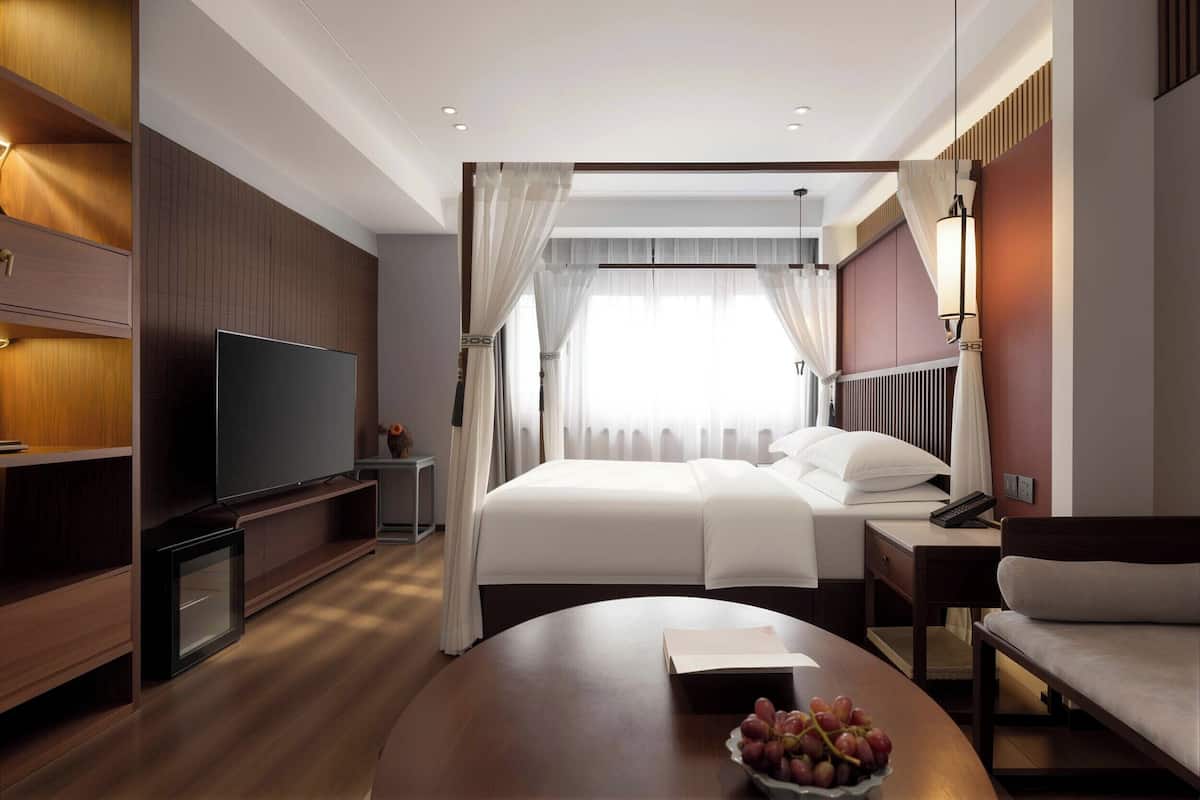 Habitación de hotel con cama, mesita de noche, televisor y una mesa redonda con un frutero.