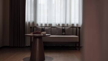 A room with a wooden floor, a round table with a white cup and a bowl of fruit, and a sofa with patterned cushions.
