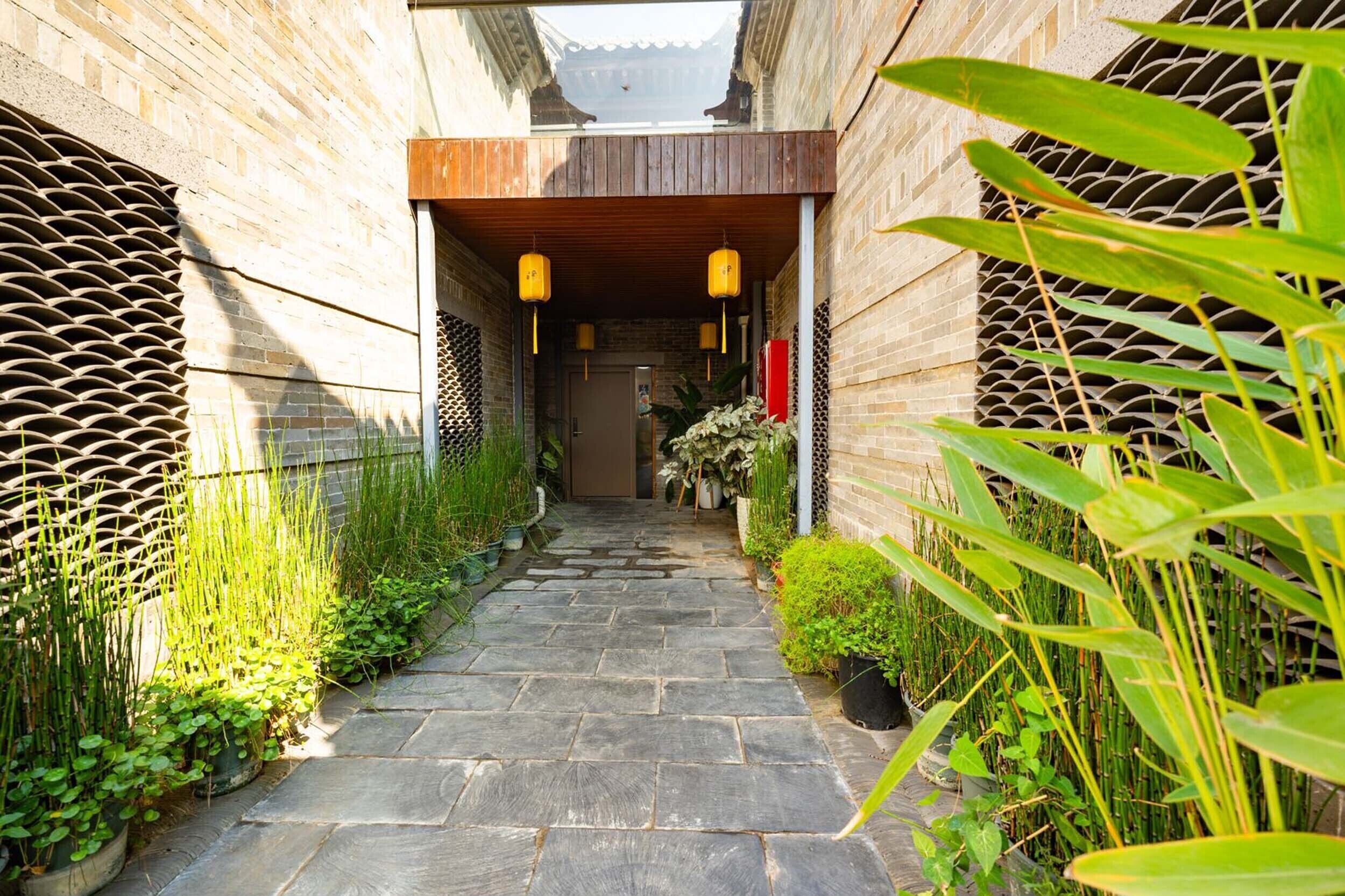 A narrow stone pathway flanked by potted plants and a wooden structure with lanterns.