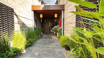 A narrow stone pathway flanked by potted plants and a wooden structure with lanterns.