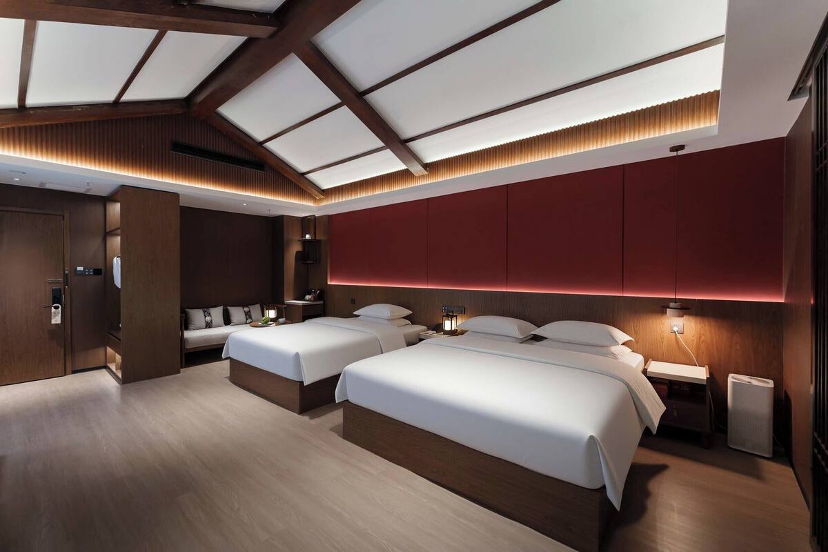 Habitación de hotel moderna con dos camas, techo de madera y una pared de acento roja.