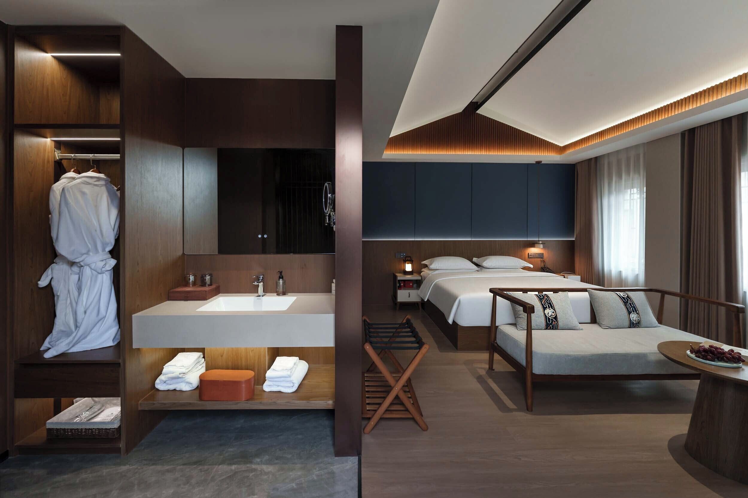 Una habitación de hotel moderna con una cama grande, un baño independiente con tocador y una zona de estar con una mesa.