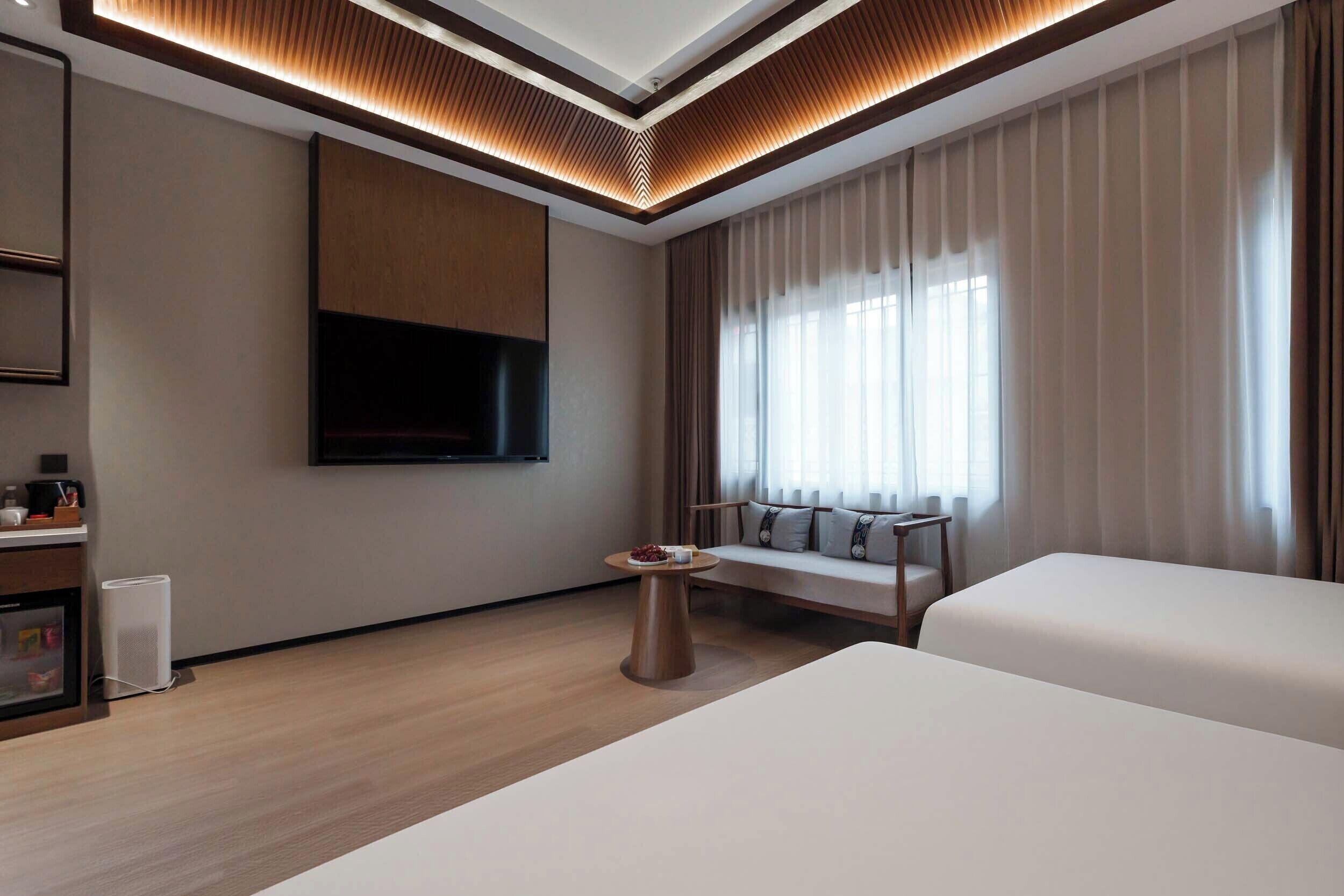 Ein modernes Hotelzimmer mit einem großen Bett, einem an der Wand montierten Fernseher, einem kleinen runden Tisch und einer Couch.