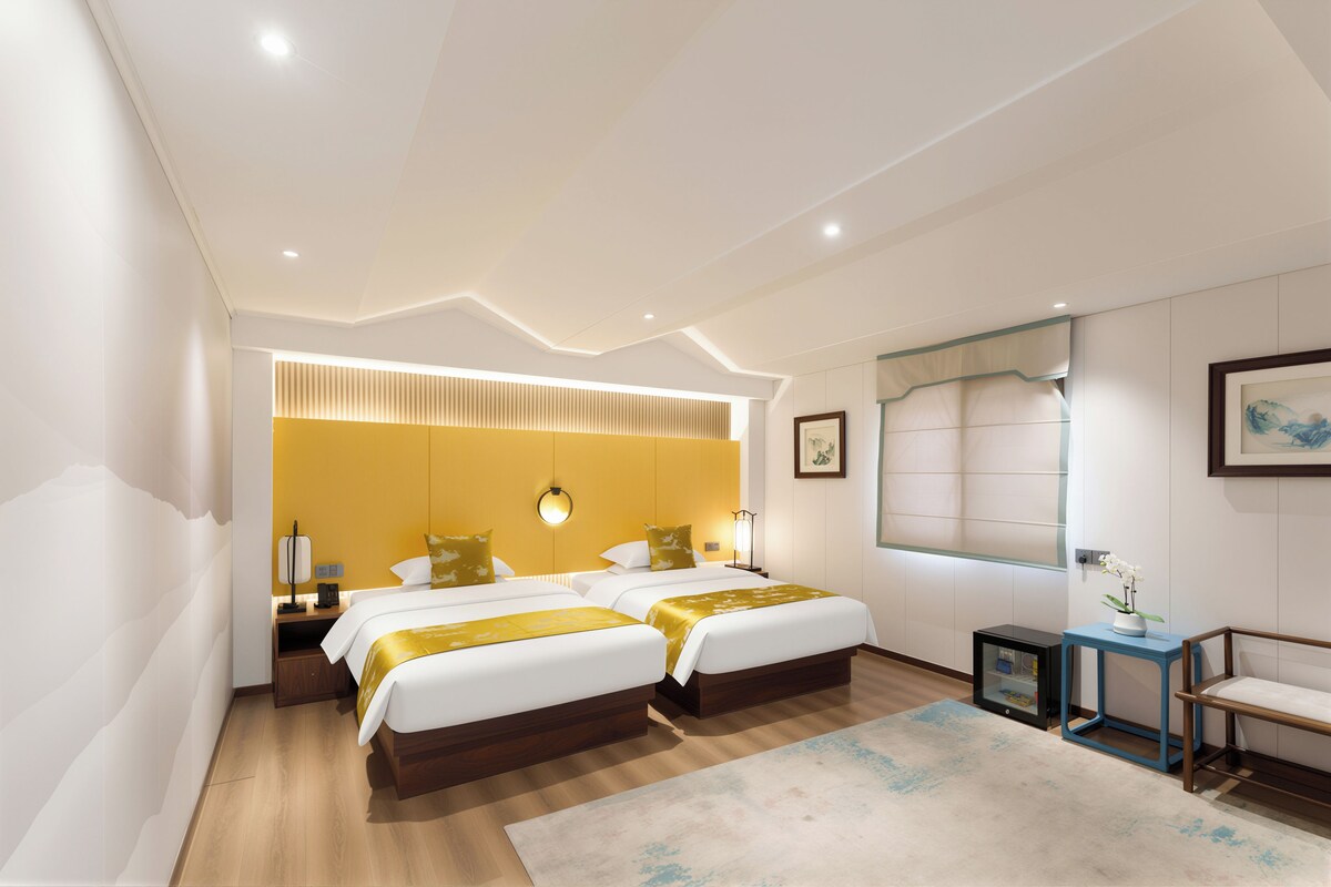 Una habitación de hotel moderna con dos camas, un ventanal grande y una mesita auxiliar.