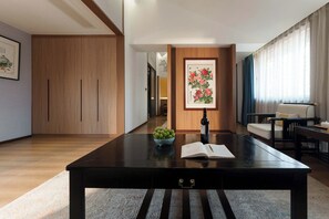 A modern living room with a wooden floor, a black table with a bowl of fruit and a book, a framed painting, and a sofa. - Luoyang Yunhuali Hotel (Luoyang)