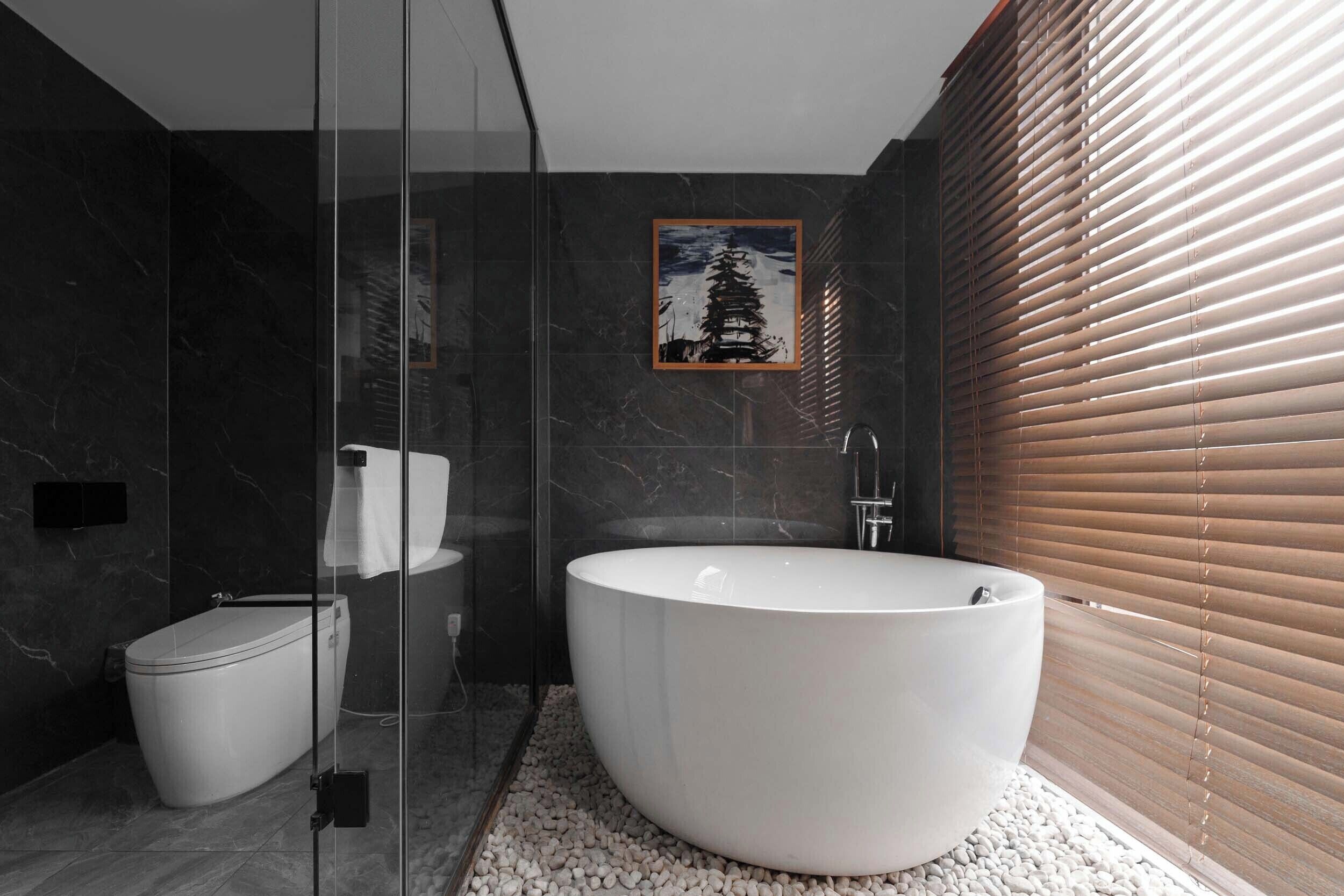 A modern bathroom with a glass-enclosed shower, a freestanding toilet, and a large freestanding bathtub.