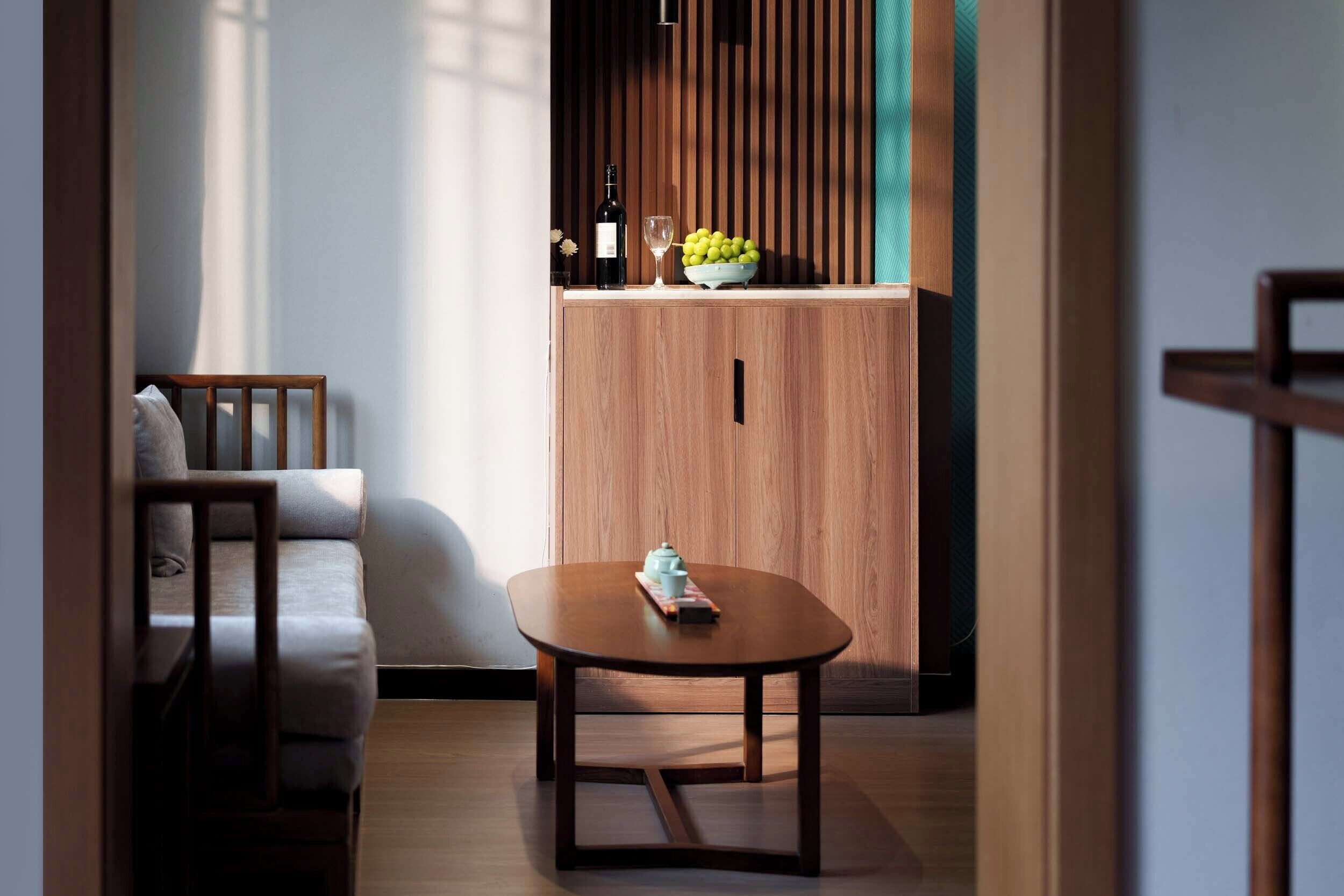 Una sala de estar moderna con un sofá de madera, una mesita y un mueble con un bol de fruta y una botella.