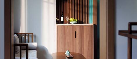 Un salon moderne avec un canapé en bois, une petite table et un meuble sur lequel se trouve un saladier rempli de fruits et une bouteille.