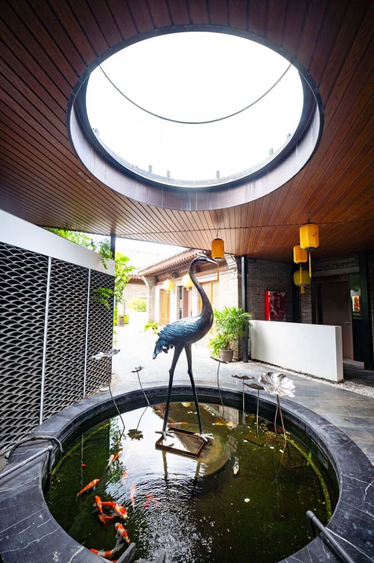 A circular skylight, a decorative bird sculpture, koi fish pond, and a reception area with a potted plant.
