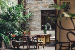 Un área de estar interior con mesas y sillas de madera, rodeada de exuberantes plantas verdes.