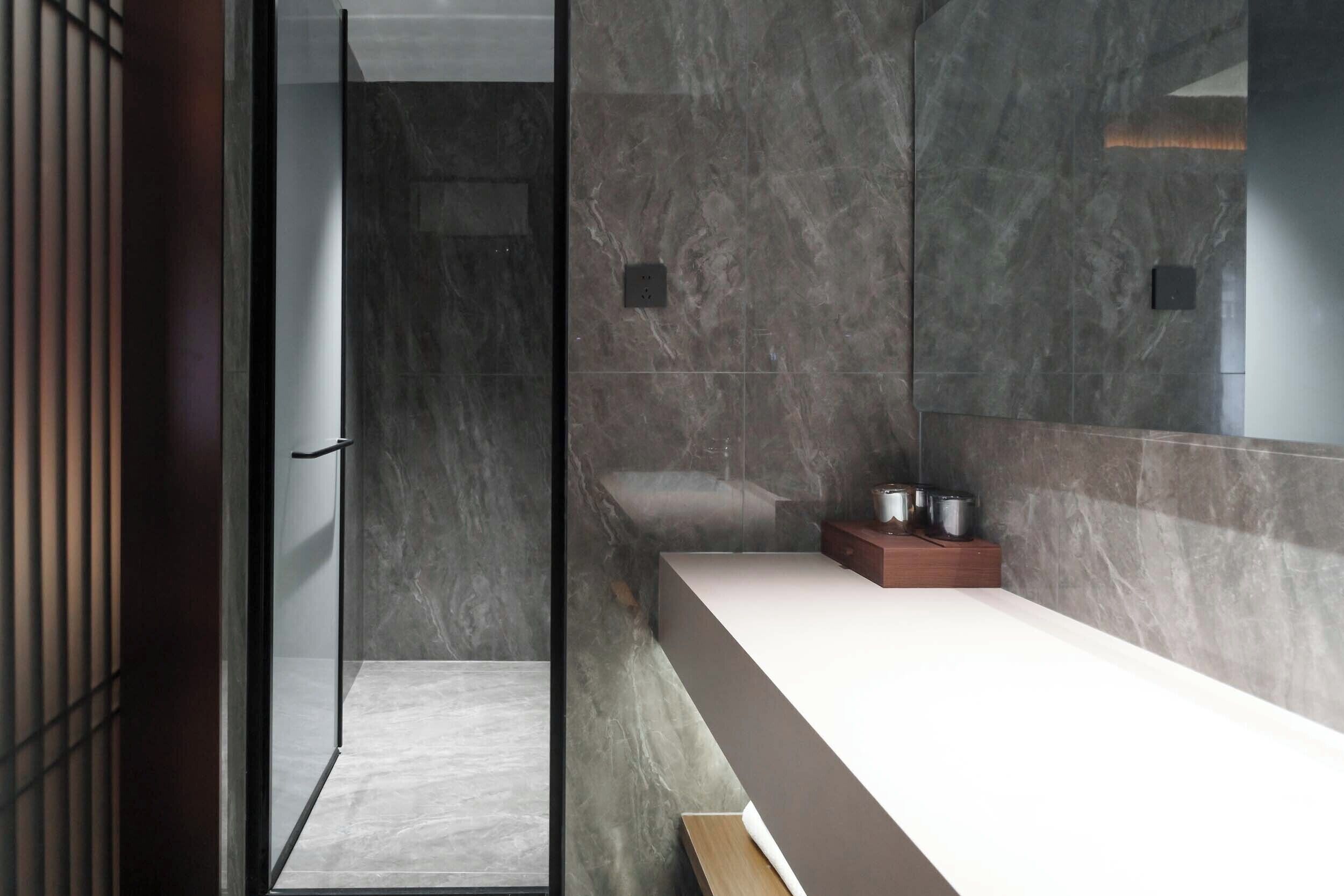 A modern bathroom with a glass shower enclosure, a white countertop, and marble walls.