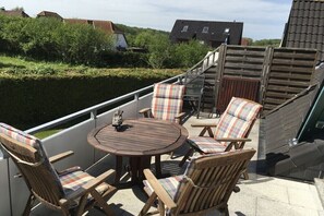 Ein Balkon mit einem runden Holztisch und vier Stühlen mit karierten Kissen.