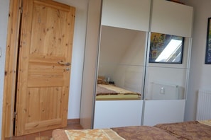 Ein Schlafzimmer mit Holztür, einem Bett mit gemustertem Überwurf, einem weißen Kleiderschrank und einem Fenster mit Aussicht.