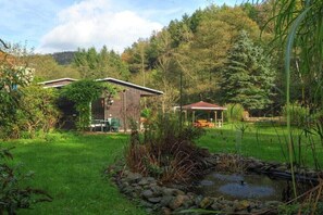 A rustic cabin with a small pond, surrounded by lush greenery and trees. - Holiday home with 2 bedrooms (Porschdorf)
