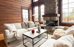 A cozy cabin interior with a stone fireplace, wooden walls, a sofa, and a coffee table.